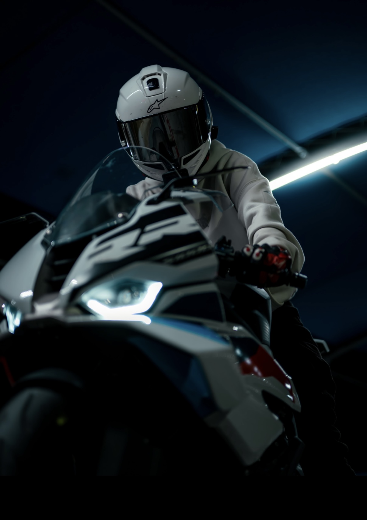 Low-angle shot of Blaze on his BMW S1000RR under a blue-lit garage canopy, headlight glowing.